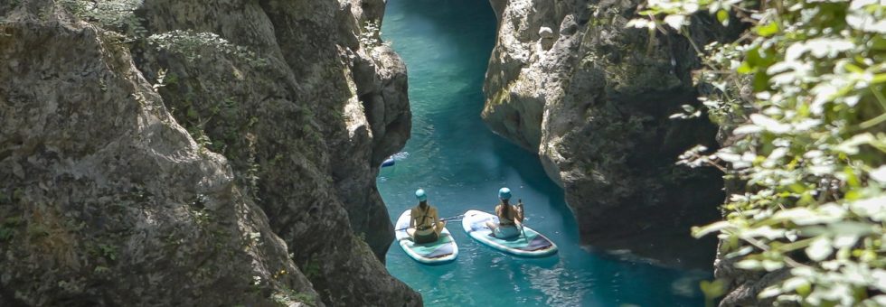 Persone in paddle board immersi nel canyon naturale del Canyon Park in Toscana, circondati da pareti rocciose e acqua cristallina