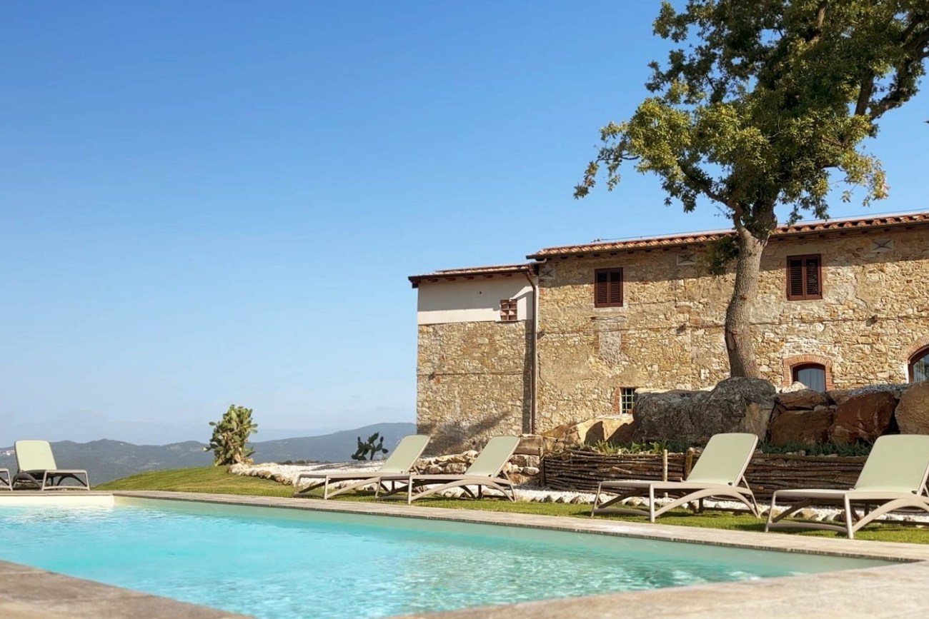 La piscina con acqua salata dell'agriturismo Poggio Belvento a Suvereto, con il casolare in pietra e la vista sulle colline della Maremma Toscana.